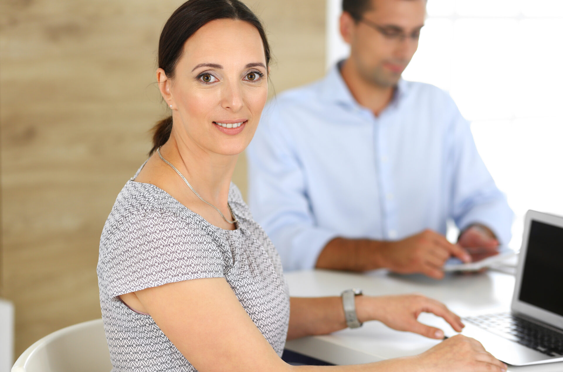 Business woman and businessman discussing questions while using a computer in modern office. Headshot of female hispanic entrepreneur at meeting. Group of diverse people. Teamwork, partnership and business concept.